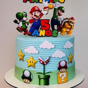 Pode incluir: Um bolo com cobertura azul-clara decorado com personagens de Super Mario, incluindo Mario, Luigi, Yoshi, Bowser e um Koopa Troopa. Um topo de bolo exibe Super Matheus 5 ANOS. As laterais apresentam recortes de nuvens, estrelas e cogumelos.