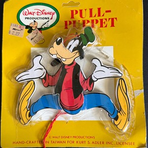 May include: Vintage Goofy pull-puppet on a yellow card. The puppet is in a jumping pose, wearing a red shirt, black vest, blue pants, and yellow shoes. The card has the Walt Disney Productions logo and the text "PULL-PUPPET".