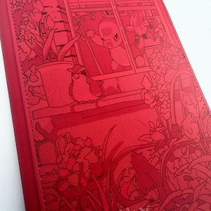 Puede incluir: Carpeta roja con una ilustración detallada. El diseño presenta un personaje de dibujos animados mirando por una ventana, rodeado de plantas y un pájaro. La obra de arte es de estilo monocromático.