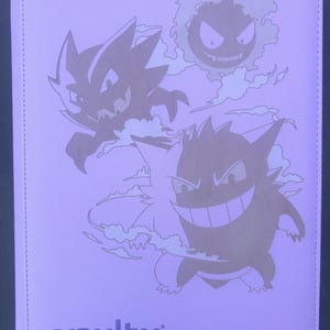 Op de afbeelding: Een paarse Vault X trading card binder met een ontwerp van drie cartoon spookkarakters. De binder heeft een gestikte rand en het Vault X-logo in de linker benedenhoek.