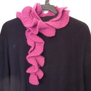 May include: A pink ruffled knitted scarf draped over a black sweater.