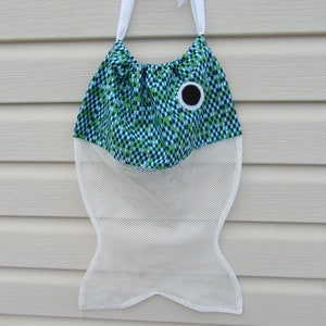 May include: A white mesh laundry bag shaped like a fish with a green and blue patterned fabric top and a black eye.