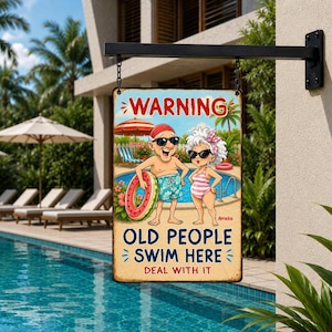 May include: A rectangular metal sign hanging from a black bracket, featuring a cartoon illustration of an elderly couple in swimwear by a pool. The text reads: WARNING OLD PEOPLE SWIM HERE DEAL WITH IT. The background shows a pool and palm trees.