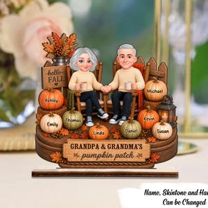 May include: A decorative wooden tabletop display featuring a cartoon-style elderly couple sitting in chairs, surrounded by pumpkins labeled with names. A sign reads hello FALL and another reads GRANDPA & GRANDMA'S pumpkin patch. Includes a lantern and autumn leaves.