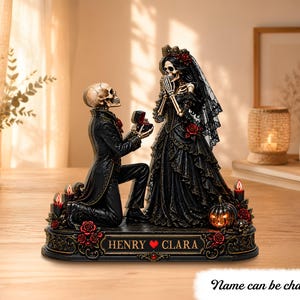 May include: A decorative figurine featuring two skeletons in formal attire. One skeleton kneels, offering an open ring box to the other. They stand on a base inscribed with the text HENRY ❤️ CLARA, surrounded by red roses, candles, and a pumpkin.