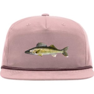 May include: A dusty rose-colored baseball cap featuring a detailed illustration of a fish. The fish is primarily olive green and yellow, with a dark grey head and tail. The cap has a brown rope detail along the brim.