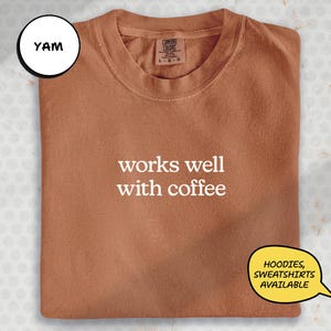 a brown t-shirt with the text "works well with coffee" printed on it.