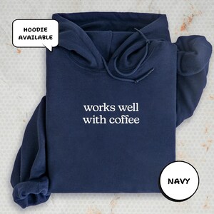 A navy blue hoodie with the text "works well with coffee" printed on it, along with a speech bubble indicating that the hoodie is available.