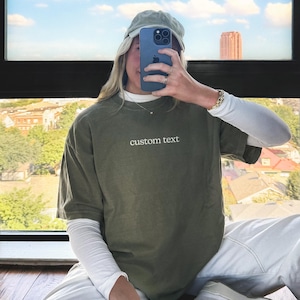 A person is sitting in front of a window, taking a selfie with a smartphone.