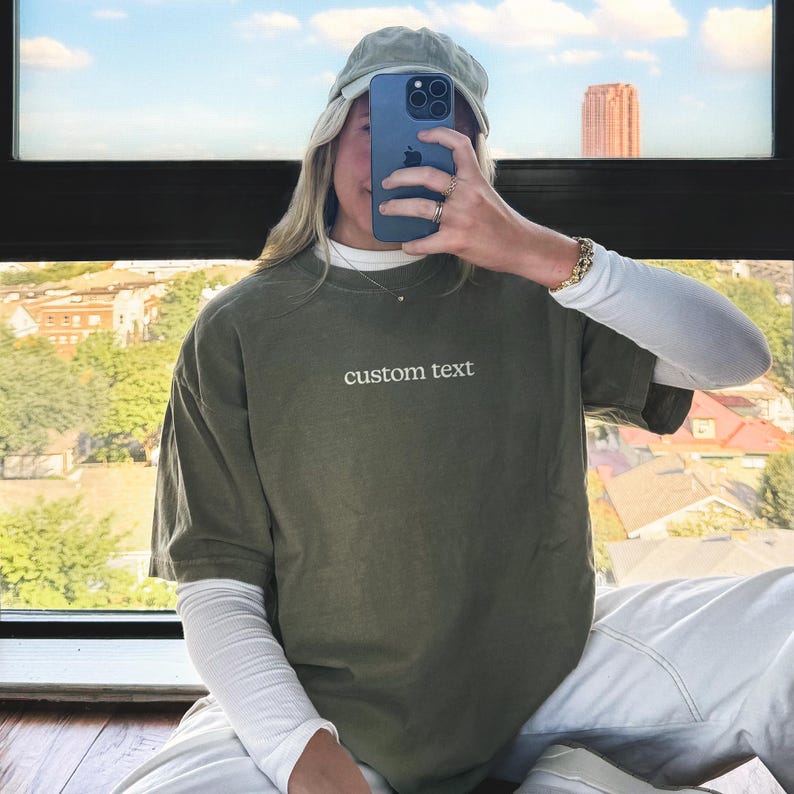 A person is sitting in front of a window, taking a selfie with a smartphone.