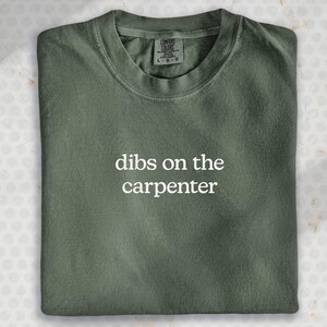 A green t-shirt with the text "dibs on the carpenter" printed on it.