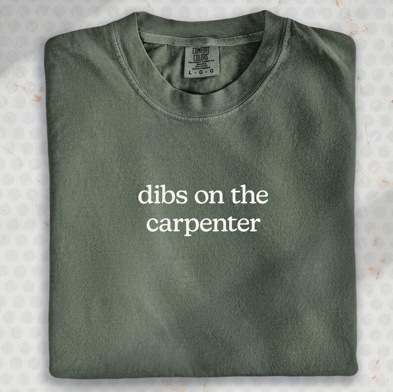 A green t-shirt with the text "dibs on the carpenter" printed on it.