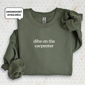 A green sweatshirt with the text "dibs on the carpenter" printed on it.