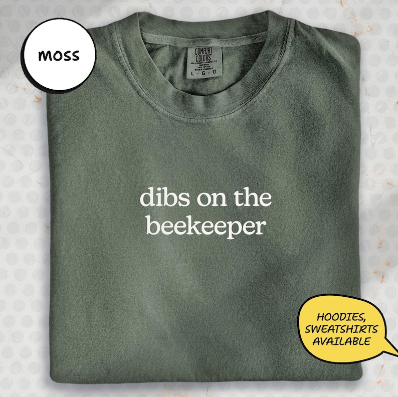 A green t-shirt with the text "dibs on the beekeeper" printed on it, along with a label on the collar.