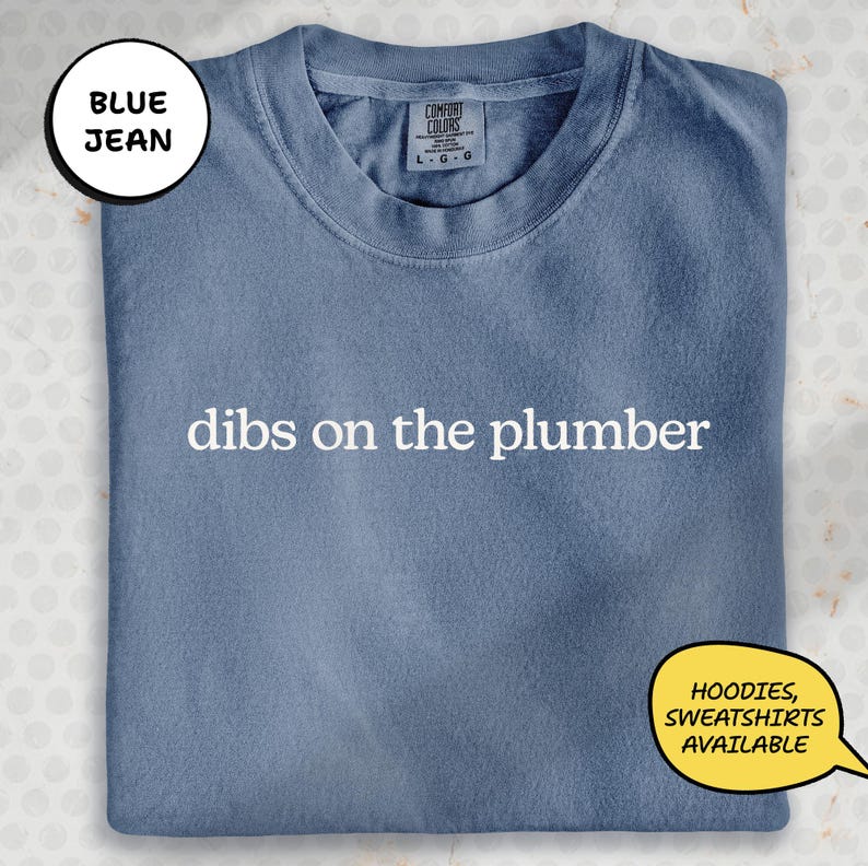 A blue t-shirt with the text "dibs on the plumber" printed on it, along with a label indicating it is a "DIBS ON THE PLUMBERS".