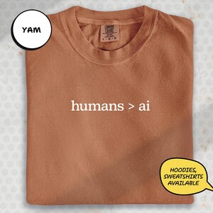 a brown t-shirt with the text "hums > ai" printed on it.