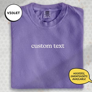 A purple t-shirt with the text "custom text" printed on it, along with a label indicating it is a custom text t-shirt.