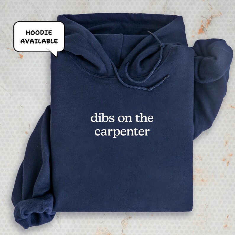 A navy blue hoodie with the text "dibs on the carpenter" printed on it, along with a speech bubble indicating that the hoodie is available.