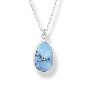 May include: A silver necklace featuring a teardrop-shaped pendant with a light blue stone. The stone displays dark, branch-like inclusions across its surface. The pendant is suspended from a delicate silver chain with a polished metal finish.