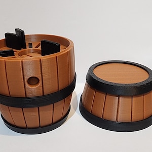 May include: A brown barrel with black bands and a removable lid. The barrel has a circular opening and several black rectangular pieces on top. The lid is also brown with a black band around the edge. The barrel is made of wood.