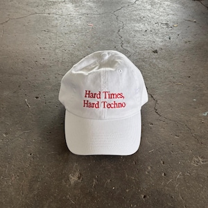 Puede incluir: Gorra de b&eacute;isbol blanca con visera curva. La gorra tiene texto bordado en rojo que dice "Hard Times, Hard Techno". El sombrero est&aacute; hecho de un material suave y es adecuado para uso casual.