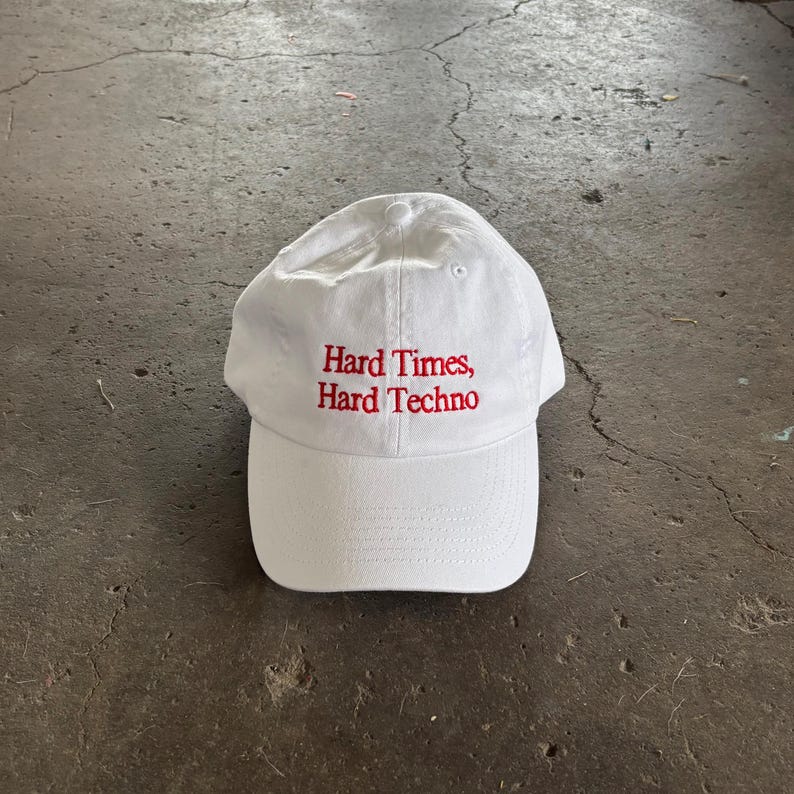Puede incluir: Gorra de b&eacute;isbol blanca con visera curva. La gorra tiene texto bordado en rojo que dice "Hard Times, Hard Techno". El sombrero est&aacute; hecho de un material suave y es adecuado para uso casual.