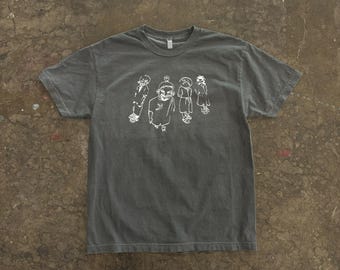 May include: Dark gray t-shirt with a crew neck. The shirt features a white graphic of five stylized figures. The figures appear to be drawn in a simple, cartoonish style. The shirt is made of a soft material.