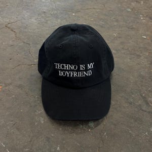 Pode incluir: Boné de beisebol preto com a frase bordada "TECHNO IS MY BOYFRIEND" em branco. O boné tem uma aba curva e um botão na parte superior. Feito de um tecido macio e durável.