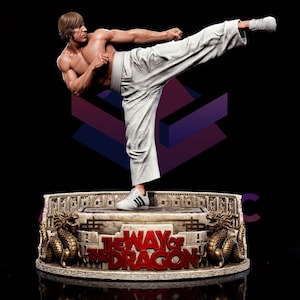 Può includere: Statua dettagliata di un artista marziale in una posa dinamica di calcio, con pantaloni bianchi e scarpe da ginnastica. La statua poggia su una base con la scritta "THE WAY OF THE DRAGON" e draghi dorati decorativi. La figura è muscolosa.