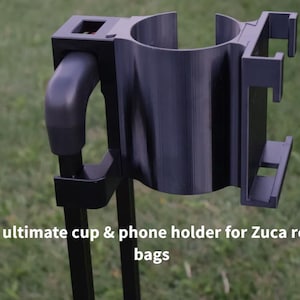 Könnte beinhalten: Ein schwarzer Becher- und Telefonhalter für Zuca-Rolltaschen. Der Halter hat einen zylindrischen Becherhalter und eine Telefonhalterung mit verstellbaren Armen. Der Text auf dem Bild lautet: "Der ultimative Becher- und Telefonhalter für Zuca-Rolltaschen."