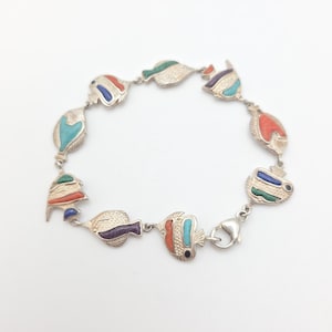 May include: Silver-toned bracelet featuring a series of colorful fish charms. Each fish is detailed with enamel in shades of red, blue, green, and purple. The bracelet has a lobster clasp closure.