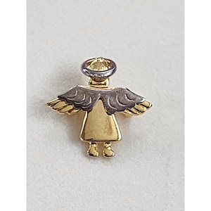 May include: A gold-toned angel pin with silver-colored wings and halo. The angel has a simple, stylized design with a triangular body and small feet. The pin is likely made of metal and is set against a neutral background.