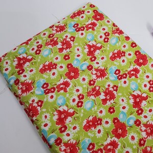 May include: Green fabric with a red and white floral pattern. The fabric has a small, repeating pattern of red flowers with white centers and green leaves. The background is a light green color.