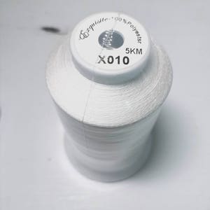 May include: A white spool of thread labeled "Exquisite 100% Polyester 5KM 010".