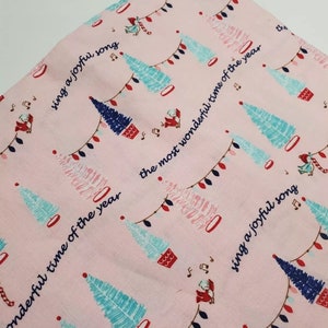 May include: Pink fabric with a repeating pattern of blue and pink Christmas trees, red and white candy canes, and white lights. The fabric has the text "sing a joyful song" and "the most wonderful time of the year" repeated throughout.