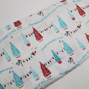 May include: White fabric with a repeating pattern of blue and red Christmas trees with white lights and birds. The text "the most wonderful time of the year" is repeated throughout the fabric.