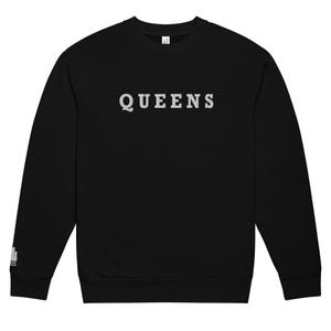 Könnte beinhalten: Schwarzes Sweatshirt mit dem Wort "QUEENS" in hellgrauer, fetter Schrift auf der Brust. Das langärmlige Oberteil hat einen Rundhalsausschnitt und eine kleine Grafik auf dem linken Ärmel. Das Sweatshirt ist aus weichem Material.