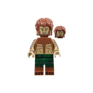 Op de afbeelding: Een Lego-minifiguur van een weerwolf met bruine vacht, een groene broek en een strenge uitdrukking. De figuur heeft een afneembaar hoofd en het ontwerp is gedetailleerd en gestileerd. De vacht van de weerwolf is getextureerd en de figuur staat op een witte achtergrond.