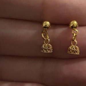 May include: A pair of gold-toned drop earrings featuring a small spherical stud connected by a single jump ring to a bell-shaped charm with an intricate, openwork filigree pattern. The earrings have a polished metallic finish and a dangling design.
