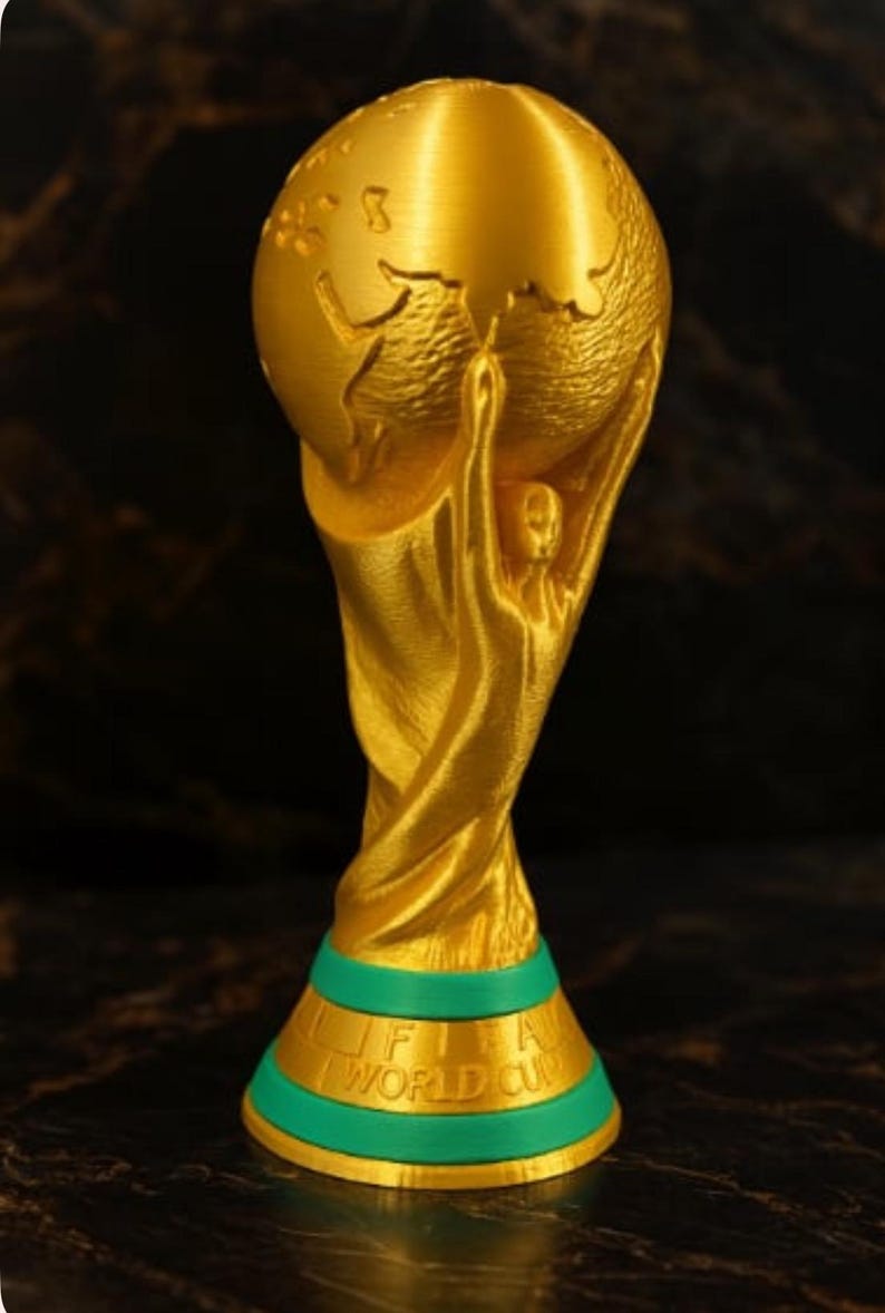 May include: A gold-colored trophy with a globe held up by two figures. The base is green with the words "FIFA WORLD CUP" in gold. The trophy is a symbol of victory and achievement.