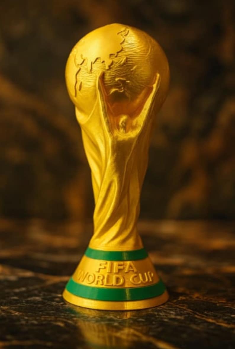 May include: A gold-colored FIFA World Cup trophy. The trophy features a globe at the top, with two figures holding it up. The base is green with the words "FIFA WORLD CUP" in gold lettering.