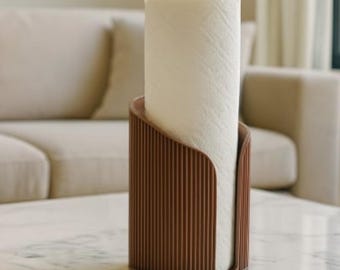 May include: A brown paper towel holder with a roll of white paper towels. The holder has a vertical, ribbed design and a curved opening. The holder is on a marble-topped table in a living room setting.