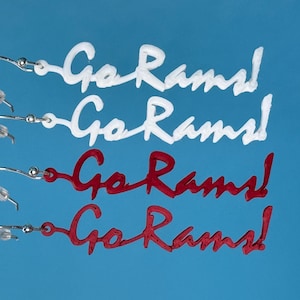 May include: White and red "Go Rams!" earrings on a blue backdrop. The earrings are in a cursive font and attached to silver-coloured ear wires. The earrings are a fan accessory.