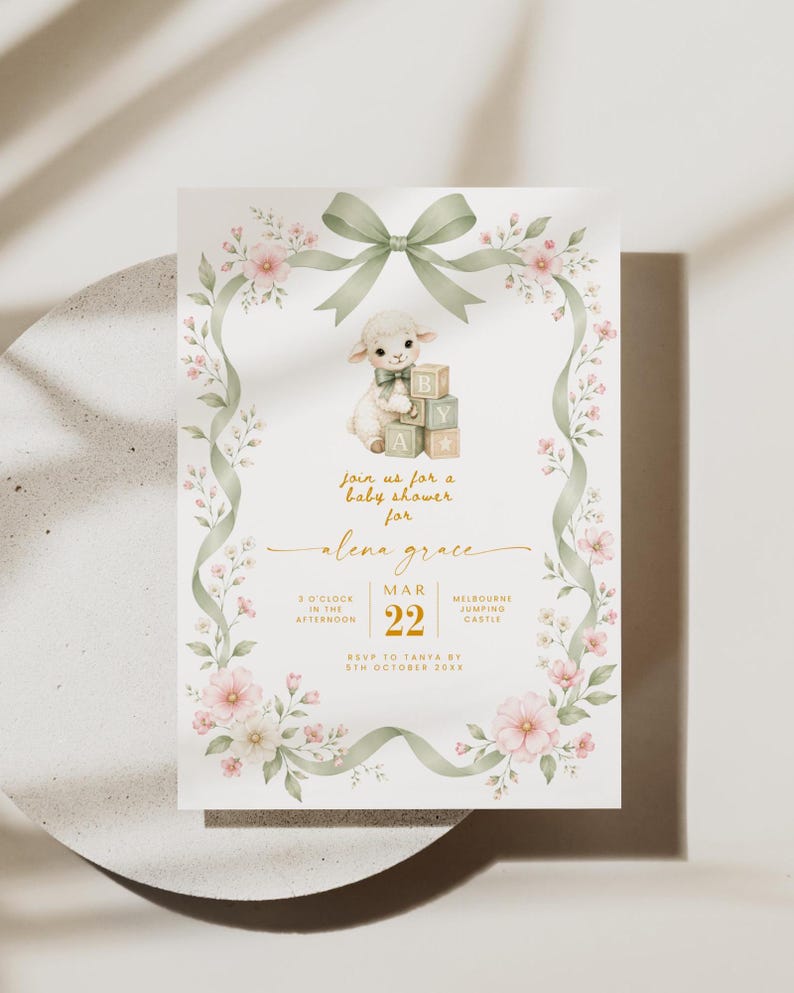 May include: A rectangular baby shower invitation card featuring a watercolor illustration of a lamb with alphabet blocks, framed by a sage green ribbon and pink floral vines. The text includes details for Alena Grace on March 22.