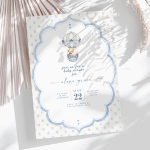 Puede incluir: Una tarjeta de invitaci&oacute;n para baby shower con fondo de lunares azul claro y un marco festoneado central. Dentro del marco hay una ilustraci&oacute;n en acuarela de un osito de peluche en un globo aerost&aacute;tico. El texto incluye Join us for a baby shower for Alena Grace, Mar 22, 3 o'clock in the afternoon, Melbourne Jumping Castle y RSVP to Tanya by 5th October 20XX.