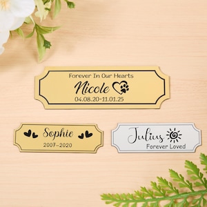 May include: Three memorial plaques with decorative edges. The top plaque is gold with the text "Forever In Our Hearts" and "Nicole" with a paw print heart. The bottom plaques read "Sophie" and "Julius".