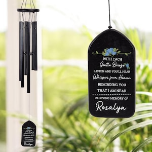 May include: Black wind chimes with a memorial plaque. The plaque has the text "WITH EACH Gentle Breeze LISTEN AND YOU'LL HEAR Whispers from Heaven REMINDING YOU THAT I AM NEAR IN LOVING MEMORY OF Rosalyn."