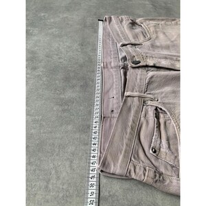 May include: A pair of light brown denim pants with a button and pocket details. A measuring tape is placed next to the pants, showing measurements in inches.
