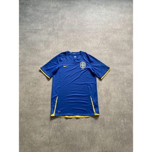 Puede incluir: Una camiseta de fútbol azul de manga corta con ribetes amarillos. La camiseta presenta un logotipo Nike amarillo y un escudo con un emblema dorado. Fabricada con un tejido ligero y transpirable.