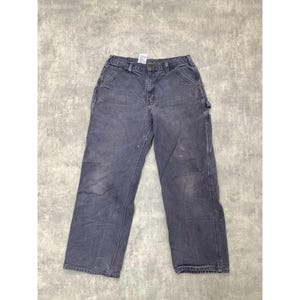 May include: Faded blue work pants with multiple pockets and a button closure. The pants show signs of wear and tear, with some white paint marks. The pants are made of a durable material, suitable for work or casual wear.